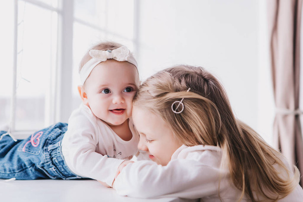 Two cute sisters sitting near window close to each other and playing. - Photo, Image
