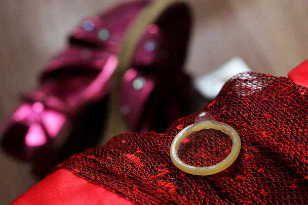 Préservatif en latex et les affaires des femmes sur le canapé si proche, chaussures roses
 - Photo, image