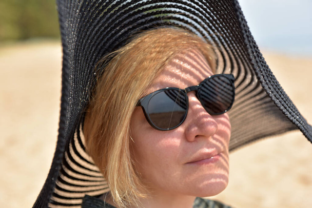 portrait of middle aged blonde woman in sunglasses and wide-brimmed hat - Фото, зображення