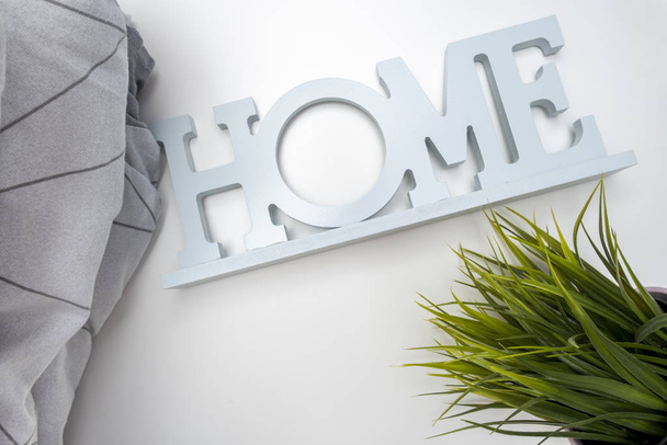 Home order background, interior details, a stack of cozy soft bedding in shades of gray, pillows and blanket with a sign home and green potted plant, home textile concept. - Φωτογραφία, εικόνα