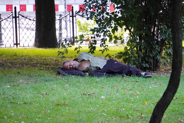 Krakow, Poland - 07.27.2019: dirty homeless man sleeps on the lawn under a tree in the Park. bums in the center of the big city. beggars - the problem of tourist cities. - Fotografie, Obrázek