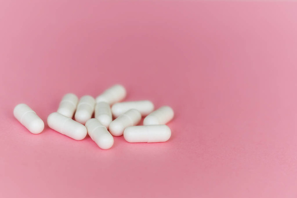 A pile of medicinal white capsules on a pink background. Free space for text. Medical background - Photo, image