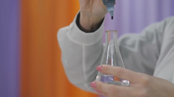 Drop of dye from the pipette falls into a flask of clear water. Preparation of liquid for the experiment. Staining the water blue. Mixing the liquid in a chemical container. - Metraje, vídeo