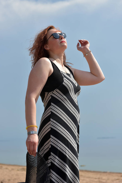vrouw van middelbare leeftijd in een gestreepte jurk op een achtergrond van de zee - Foto, afbeelding