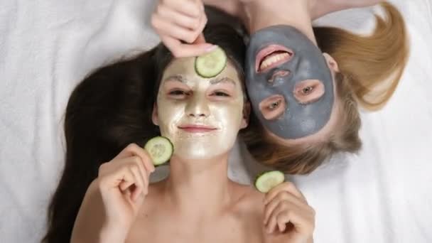 Vista superior de las mujeres jóvenes con máscara facial y tratamiento de pepino en las caras tienen relajarse en el centro de bienestar. Concepto de cuidado de la piel, cosméticos, salón de belleza, tratamiento facial, masaje facial, bienestar y
 - Metraje, vídeo