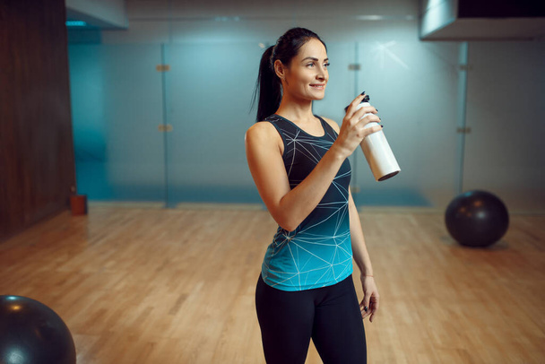 Mujer sonriente bebe agua después del entrenamiento de pilates en el gimnasio, estilo de vida saludable. Fitness workuot en el club deportivo. Persona atlética femenina, aeróbic interior, estiramiento corporal
 - Foto, Imagen