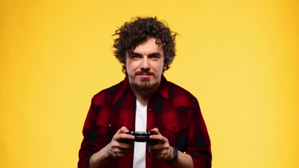 Nerdy gamer with controller on yellow background. Man with curly hair - Felvétel, videó