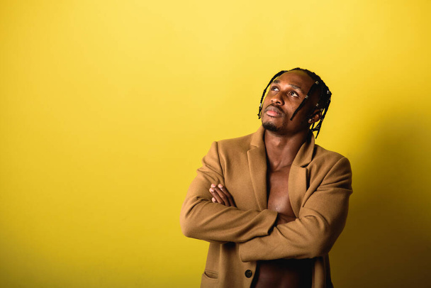 portrét mladého černocha, africký vzhled, emocionální a vážný a vzhlížející, s dredy, na žlutém pozadí - Fotografie, Obrázek