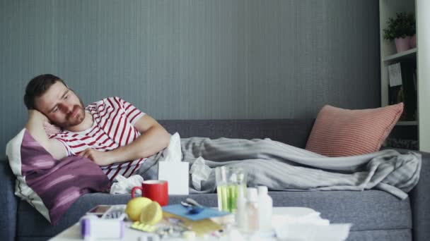 Homme malade avec la grippe couché sur le canapé à la maison. Jeune homme malade avec température de contrôle à froid avec thermomètre
 - Séquence, vidéo