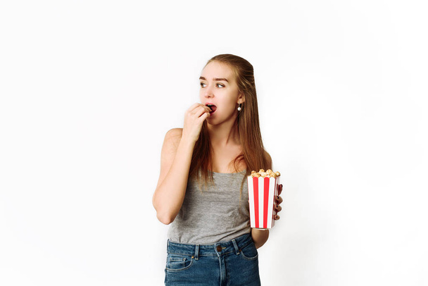 Kaunis blondi tyttö syödä popcornia ja katsella elokuvan eristetty valkoisella taustalla. Kopioi Space, malli blogi ja mainonta. Nainen pitää popcornia ja katsoo oikein.
. - Valokuva, kuva