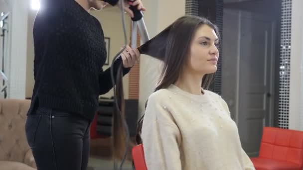 Fryzjer stosujący szczypce do włosów i grzebień do fryzury w salonie piękności. Close-up fryzjer robi falowane włosy z szczypcami w salonie fryzjerskim. 4k wideo - Materiał filmowy, wideo