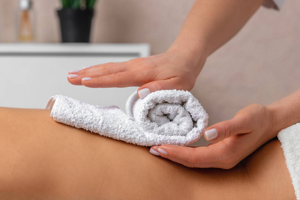 female masseur hands putting white towel on the back of young woman enjoying treatment procedure in spa salon, atmosphere of calm and relaxation, concept of massage, body care and beauty - Фото, зображення