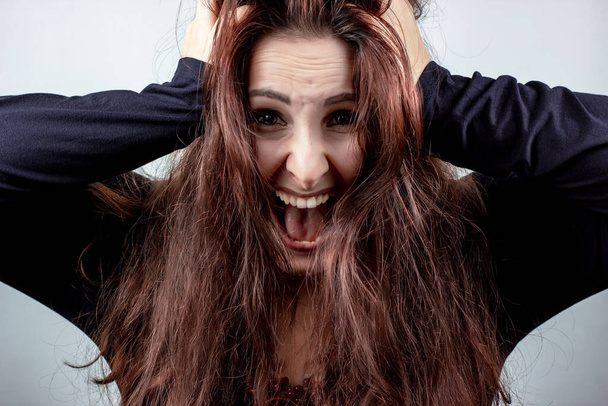 Στρεσαρισμένη, φοβισμένη και ουρλιάζοντας ελκυστική νεαρή τρελή γυναίκα με μαύρα σε ανοιχτό φόντο - Φωτογραφία, εικόνα