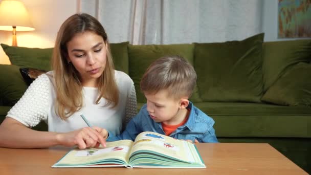 Attractive mother and son studying together at home. Home education concept. Nanny teaching a boy at home doing homework. - Footage, Video