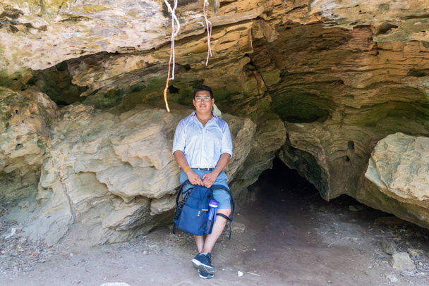 Egy fiatal férfi portréja egy barlang előtt, alkalmi ruhában és hátizsákkal a kezében. - Fotó, kép