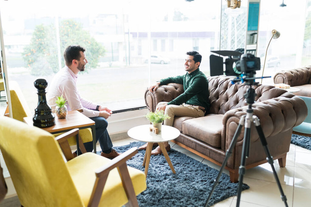 Reportero masculino sentado con un joven profesional mientras graba la entrevista en la oficina
 - Foto, Imagen