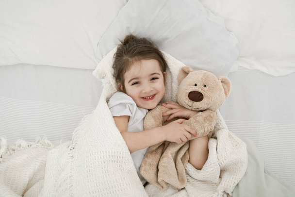 かわいい女の子がテディベアのおもちゃでベッドで寝ています。子供の発達と睡眠の概念。上からの眺め. - 写真・画像
