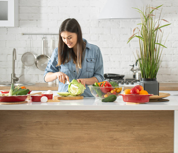 Een jonge mooie vrouw bereidt een salade van verschillende groenten in de keuken. Het concept van een gezonde voeding en levensstijl. - Foto, afbeelding
