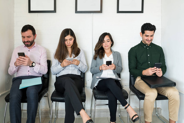 Buscadores de empleo masculinos y femeninos usando teléfono móvil mientras están sentados para una entrevista en la oficina
 - Foto, Imagen
