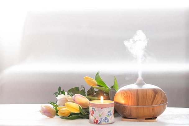 Aromatický olej difuzor lampa na stole na rozmazaném pozadí s krásnou jarní kytice tulipánů a hořící svíčky . - Fotografie, Obrázek