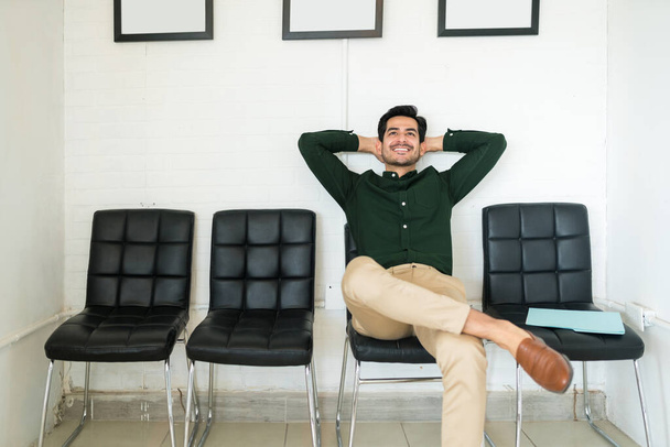 Candidato sonriente reflexivo sentado en la sala de espera para la entrevista de trabajo en la oficina
 - Foto, imagen
