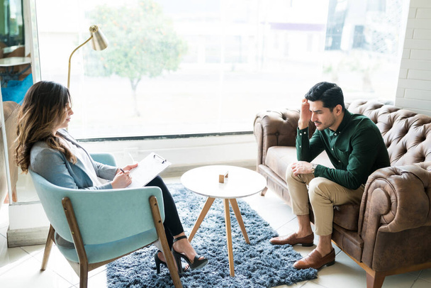 Женщина-консультант дает советы депрессивному латинскому мужчине во время сеанса терапии в офисе
  - Фото, изображение