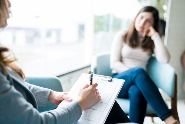 Vrouwelijke therapeut die op notitieblok schrijft tijdens een gesprek met de patiënt op kantoor tijdens de psychologie behandeling - Foto, afbeelding