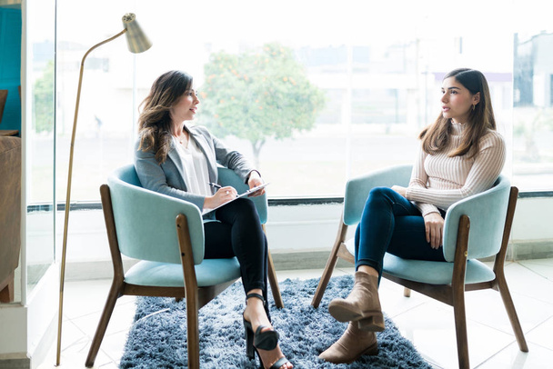 Young woman sharing her problems with female therapist during psychotherapy session in office - Fotoğraf, Görsel