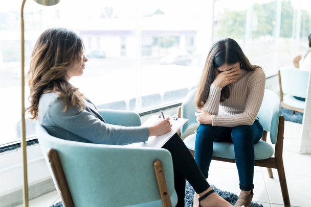 Mujer joven deprimida llorando mientras discute sus problemas con el psicólogo en el consultorio
 - Foto, Imagen