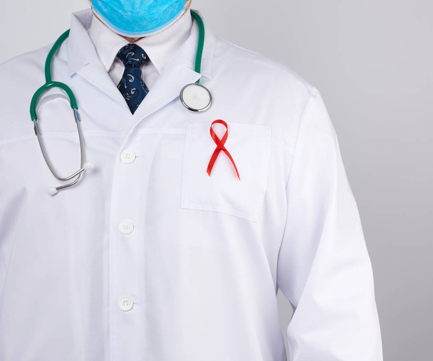 doctor in a white coat and tie is standing on a white background, red silk ribbon is hanging on his chest, symbol of the fight against disease AID - Φωτογραφία, εικόνα