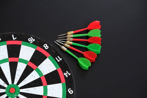 dart sporu dalı, dart tahtası ve siyah zeminde renkli dart okları - Fotoğraf, Görsel