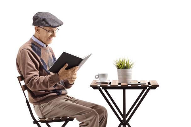 Mature man reading a book and sitting at a table isolated on white background - Foto, afbeelding