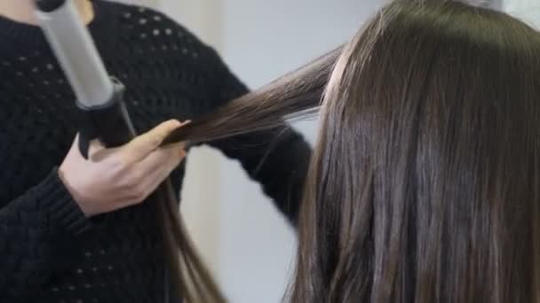 Процесс кёрлинга длинных волос с щипцами для волос в современной студии красоты. Крупный план женской парикмахерской с использованием утюга для волос. Парикмахер делает стильную прическу. Макро. 4k кадров
 - Кадры, видео
