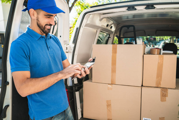 Portrait of a delivery man checking the products in checklist while standing right next to his van. Delivery and shipping concept. - Photo, image