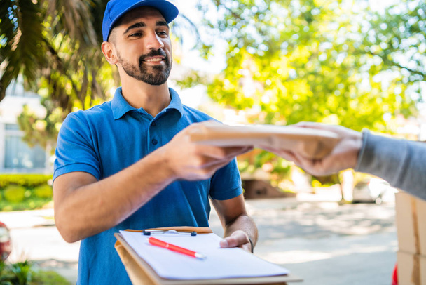 Portrait of a delivery man making home delivery to his customer. Delivery and shipping concept. - Photo, Image