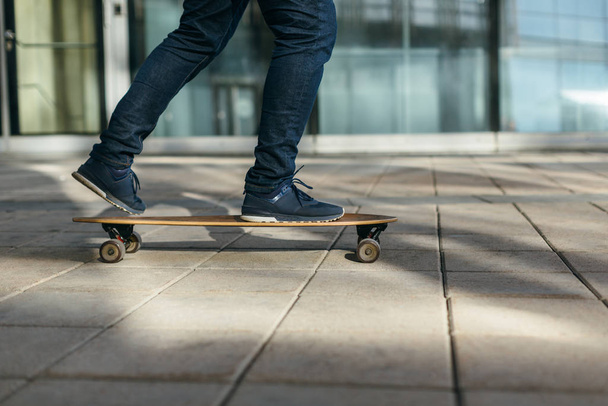 Man skateboarding in city with one foot placed on board and pushing off with the other. Riding on longboard on paving stone. Selective focus on skateboard. Concept of leisure activity and urban. - Fotó, kép