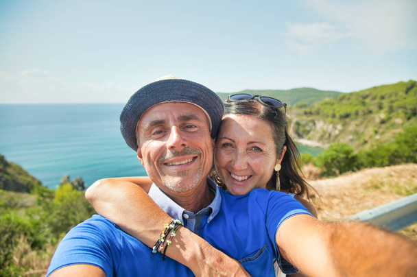 Άντρας που φοράει ψάθινο καπέλο με τη γυναίκα του να χαλαρώνει στη θάλασσα, ωκεανός στο βάθος. - Φωτογραφία, εικόνα