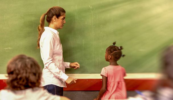 緑の黒板の前で先生と一緒に小学校のアフリカ人の女の子. - 写真・画像