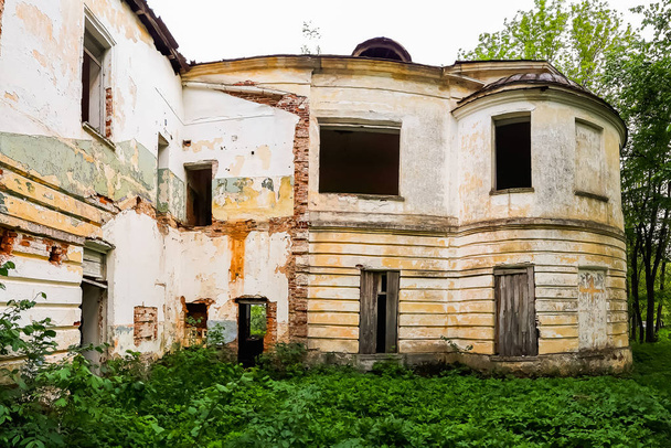 Altes verlassenes Herrenhaus mit vergitterten Fenstern. Der Bau eines alten verlassenen Herrenhauses inmitten grüner Bäume - Foto, Bild
