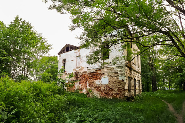 Altes verlassenes Herrenhaus mit vergitterten Fenstern. Der Bau eines alten verlassenen Herrenhauses inmitten grüner Bäume - Foto, Bild