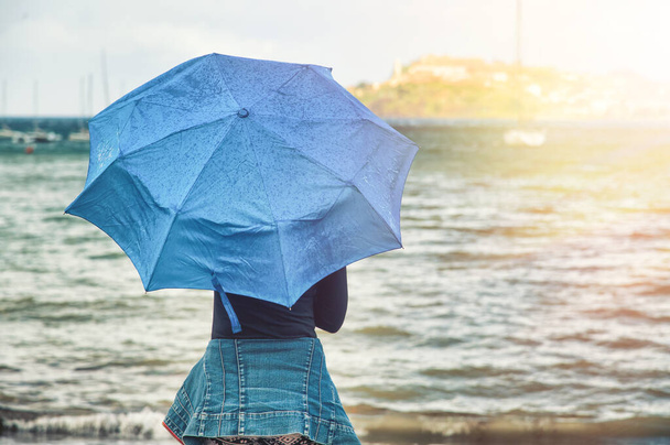 Kobieta trzymająca niebieski parasol relaksujący nad morzem, ocean w tle, widok z tyłu - Zdjęcie, obraz