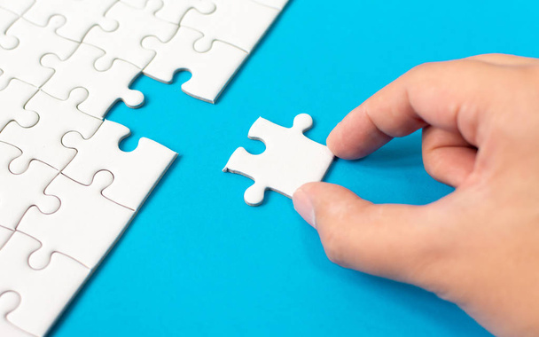 Hand putting piece of white jigsaw puzzle on blue background. Team business success partnership or teamwork. - Foto, immagini