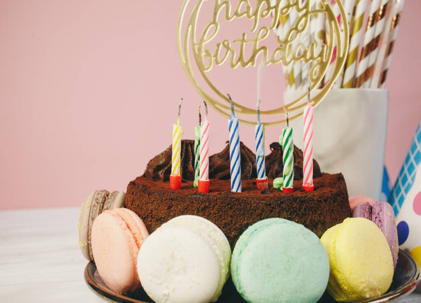 Fresco cholocate deliziosa torta con maracoons intorno ad esso con topper Buon compleanno sul tavolo sullo sfondo rosa. Da vicino.
.  - Foto, immagini