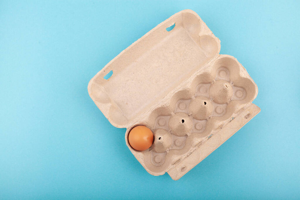 Eieren Kippeneieren. Bovenaanzicht van een open grijze doos met bruine eieren geïsoleerd op een blauwe achtergrond. Het concept van een gezonde levensstijl, het krijgen van pure eiwitten. Goed ontbijt. Eén ei.. - Foto, afbeelding