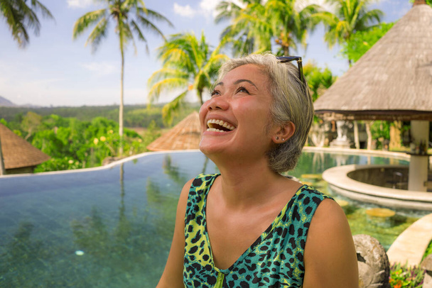 outdoors lifestyle photo of middle aged attractive and relaxed woman with grey hair enjoying happy the beautiful view from tropical resort infinity pool in exotic and luxury holiday travel - Foto, imagen