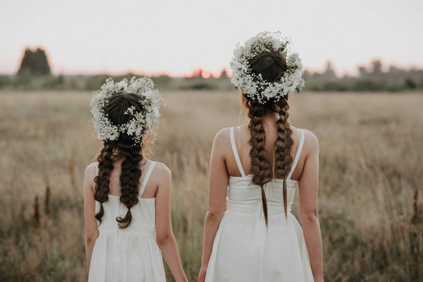 мати і дочка спини в білих сукнях з косами і квітковими вінками в стилі бохо влітку
 - Фото, зображення