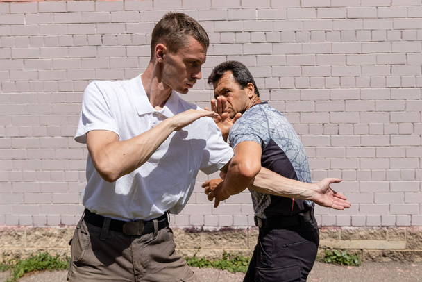 Martial arts instructors Krav Maga demonstrate self-defense techniques in a street fight. . Defender blocks the attacker's hand and deals a counter strike - Foto, imagen