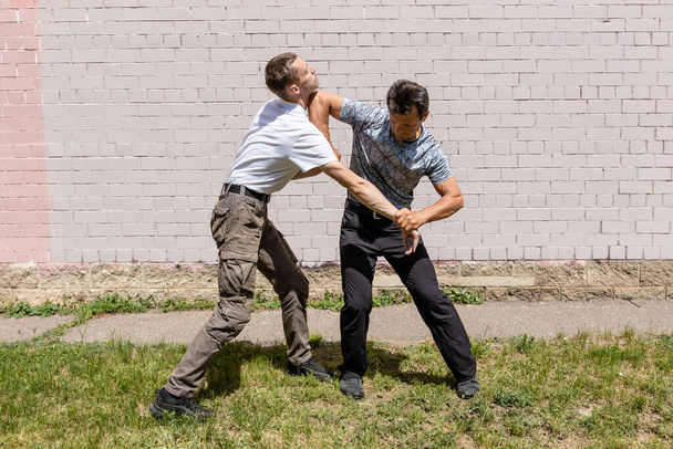 Martial arts instructors Krav Maga demonstrate self-defense techniques in a street fight. . Defender blocks the attacker's hand and deals a counter strike with the elbow of his face - Foto, Imagen