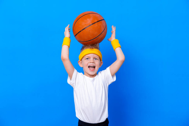 Sporty little boy with basketball ball over blue studio background. Gym workout. Child sportsman. Activity. Sport. Fitness, health and energy. Success - Foto, afbeelding