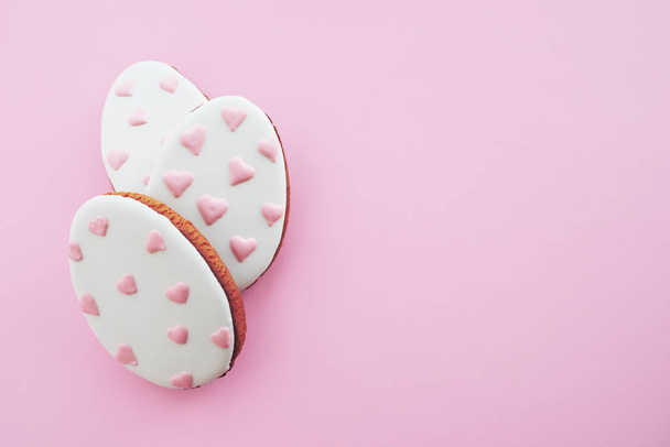 Three egg-shaped gingerbread cookies with painted pink hearts in a row against a pink background. Easter concept - Foto, imagen